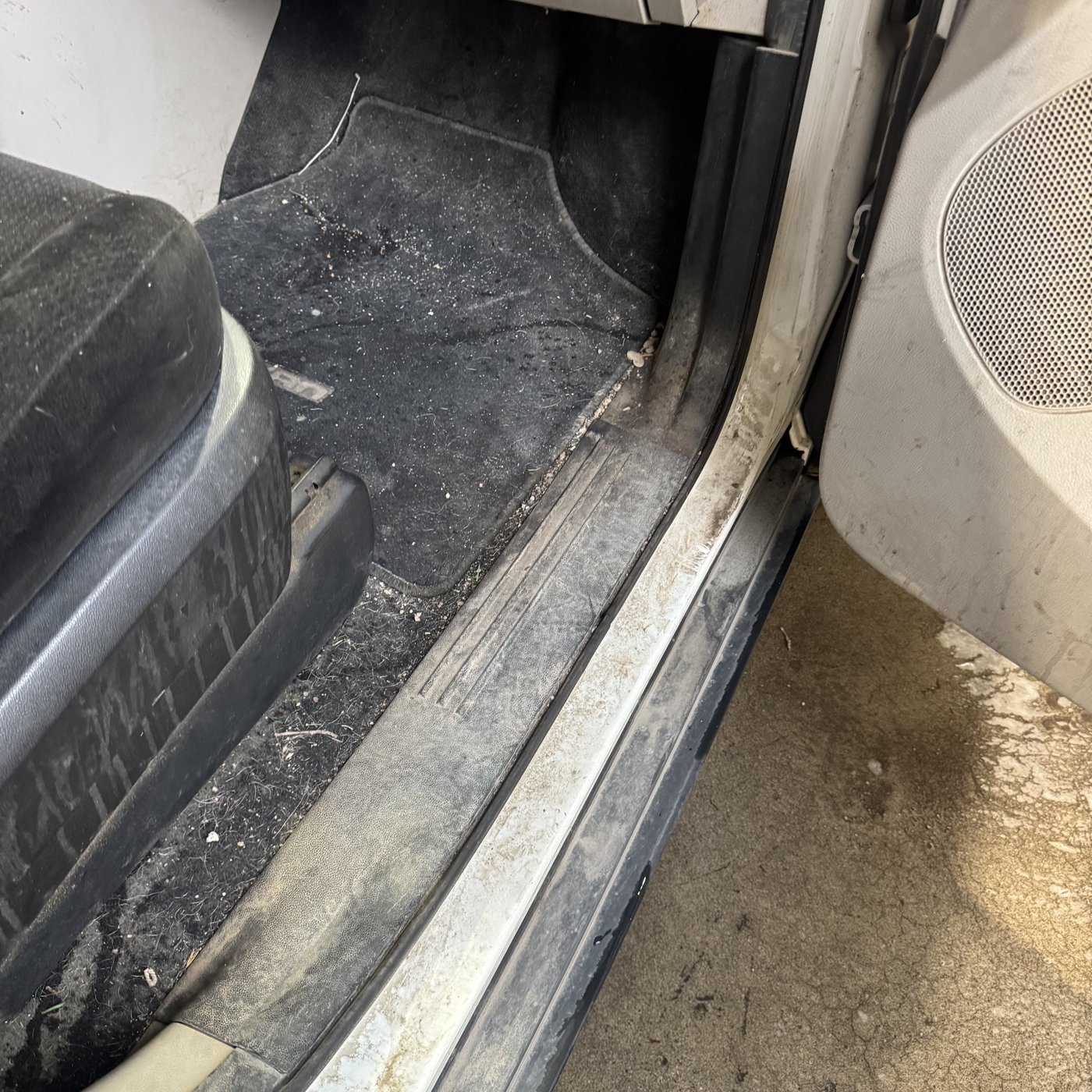 Footwell and door sill before detailing, with dirt and debris on the carpet
